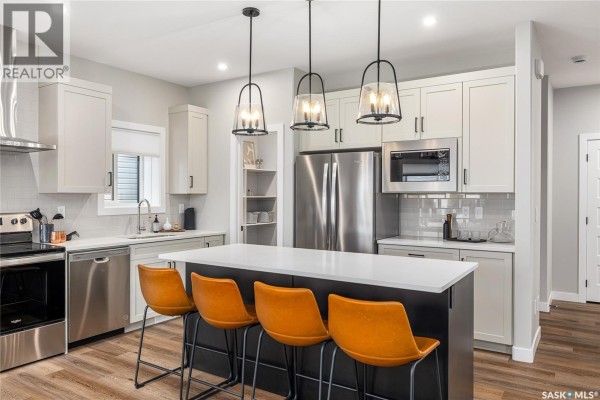 Kitchen featuring light gray cabinets, stainless steel appliances, and a large central island with seating. - 3012 Favel Drive, Regina