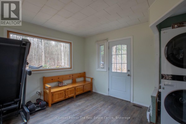 Room featuring a treadmill, wooden bench, door to the outside, and stacked washer and dryer. - 3016 118 Highway, Bracebridge