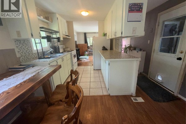 View of a mobile home kitchen and adjacent room with wood floors and a dining table with chairs. - 3018 Perrier Road Unit# 14, Nelson