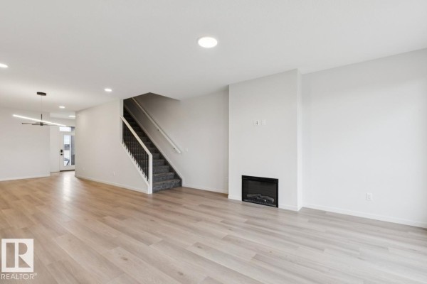 Living room with light wood floors, white walls, a fireplace, and a staircase. - 3019 5 Av Sw, Edmonton