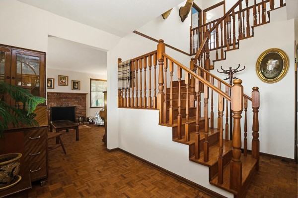 Foyer with a wooden staircase, wood-paneled floor, and a view into a living room with a brick fireplace. - 30199 Silverdale Avenue, Mission