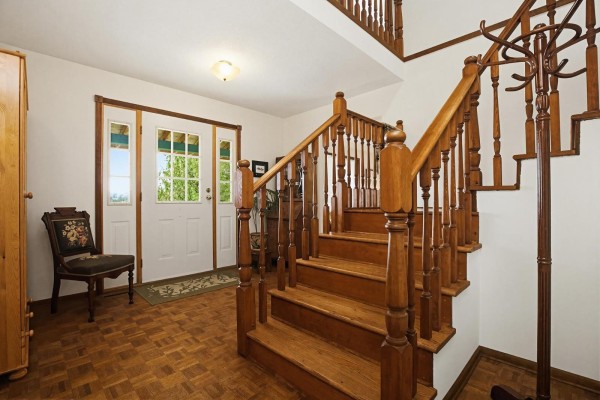 Front foyer with a wooden staircase, white double doors, and a patterned upholstered chair beside a wooden cabinet. - 30199 Silverdale Avenue, Mission