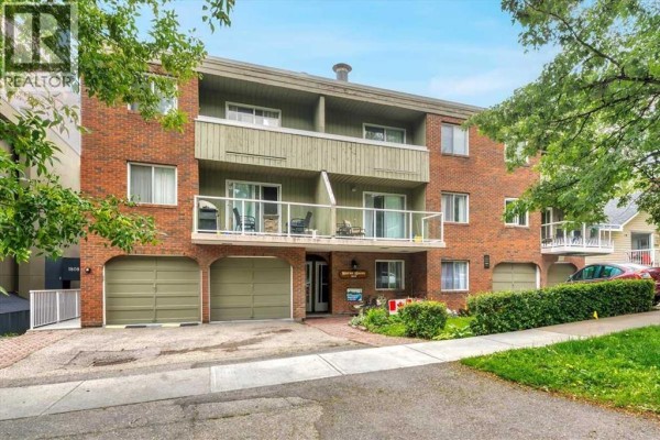 Front view of the apartment building with brick exterior, balconies, and green garage doors. - 302, 1814 18 Street Sw, Calgary