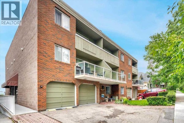 Side angle of the apartment building showing brick facade, balconies, and green garage doors. - 302, 1814 18 Street Sw, Calgary