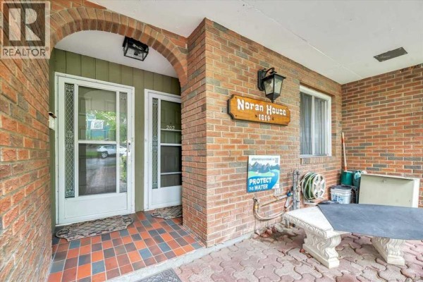 Entrance area of the apartment building with brick columns, glass doors, and a 'NORAN HOUSE' sign. - 302, 1814 18 Street Sw, Calgary
