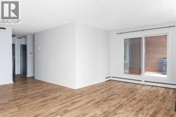 Empty living room with white walls, a sliding glass door leading to a patio, and wood laminate flooring. - 302, 2611 15a Street Sw, Calgary