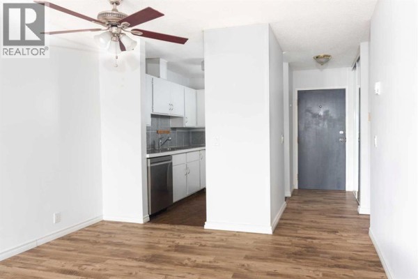 Combined living and kitchen area with white cabinets, stainless steel appliances, and a ceiling fan. - 302, 2611 15a Street Sw, Calgary