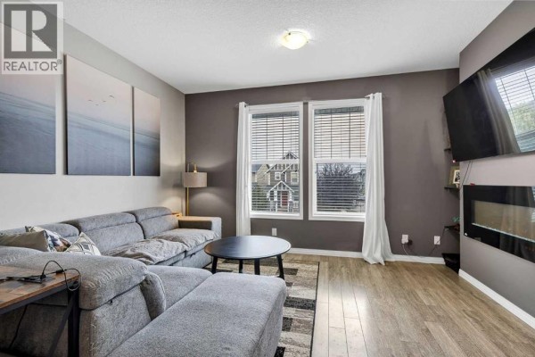 Living room with a gray sectional sofa, round coffee table, and wall-mounted TV. - 302, 280 Williamstown Close Nw, Airdrie