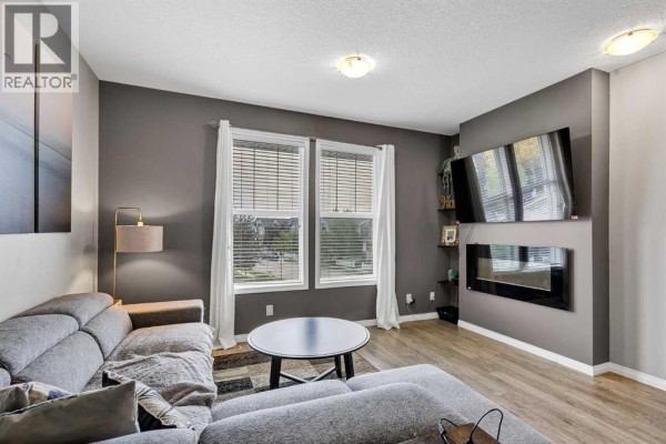 Living room showcasing a fireplace, gray sofa, and large windows with blinds. - 302, 280 Williamstown Close Nw, Airdrie
