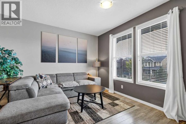 Living area with a sectional sofa, coffee table, and three large windows overlooking a street. - 302, 280 Williamstown Close Nw, Airdrie