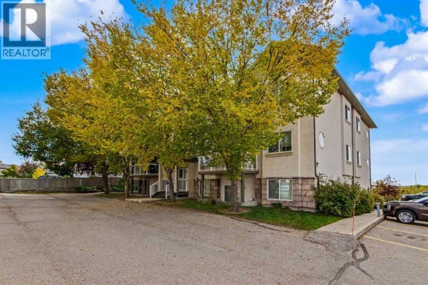 Side exterior of a three-story apartment building with a parking lot, concrete base, and trees. - 302, 7 Crystal Ridge Cove, Strathmore