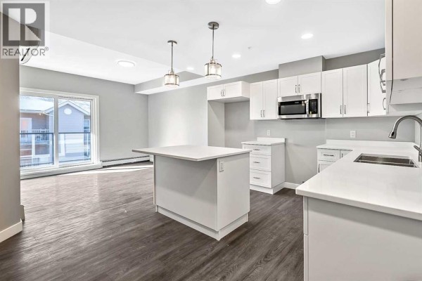 Open-concept kitchen and living area with large windows, island, and modern cabinetry. - 302, 97 Station Drive, Sylvan Lake