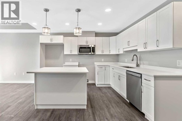 Close-up of kitchen with white cabinets, stainless steel appliances, and pendant lighting. - 302, 97 Station Drive, Sylvan Lake