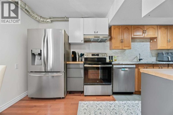 View of the kitchen including a large refrigerator, stainless steel oven, and dishwasher. - 302, 9930 Bonaventure Drive Se, Calgary