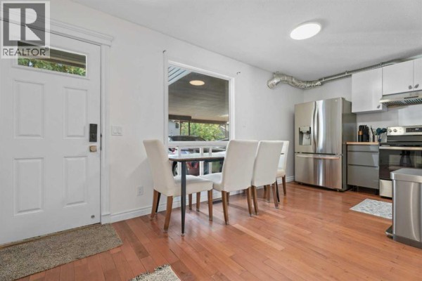Dining area with white chairs around a dark table next to the kitchen. - 302, 9930 Bonaventure Drive Se, Calgary