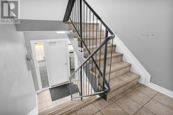 Interior staircase with beige tiled steps, grey walls, and a black metal railing leading down. - 302 - 1005 Laurier Street, Clarence Rockland
