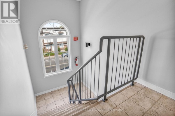 View down a staircase with beige tiles, grey walls, and an arched window overlooking a street. - 302 - 1005 Laurier Street, Clarence Rockland