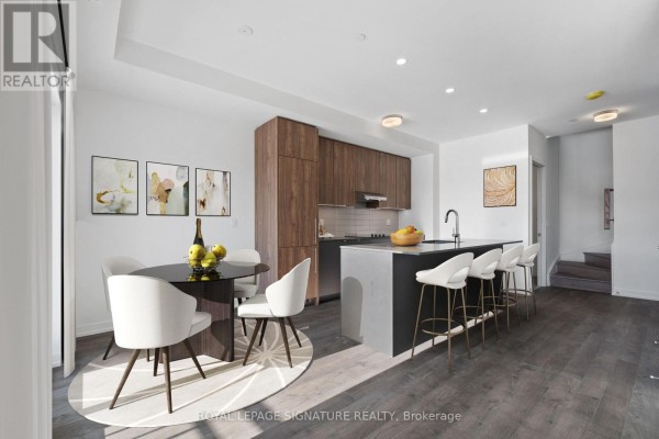 Open concept dining area with round table and modern kitchen with island. - 302 - 11 Walder Lane, Richmond Hill