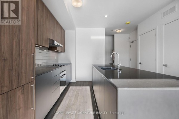 Modern kitchen with dark wood cabinets, stainless steel appliances, and island. - 302 - 11 Walder Lane, Richmond Hill