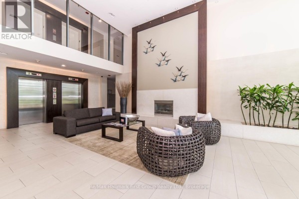 Apartment building lobby with elevators, seating area, fireplace, and decorative art. - 302 - 1600 Charles Street, Whitby