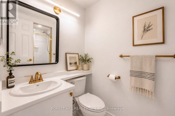 A white bathroom with a vanity, sink, toilet, mirror, and gold-toned fixtures. - 302 - 1818 Bayview Avenue, Toronto