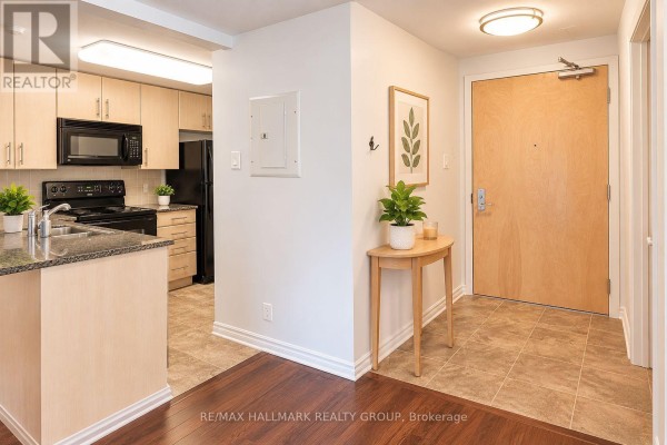 Apartment entryway with a wood door, tiled floor, and a small console table. - 302 - 200 Lett Street, Ottawa