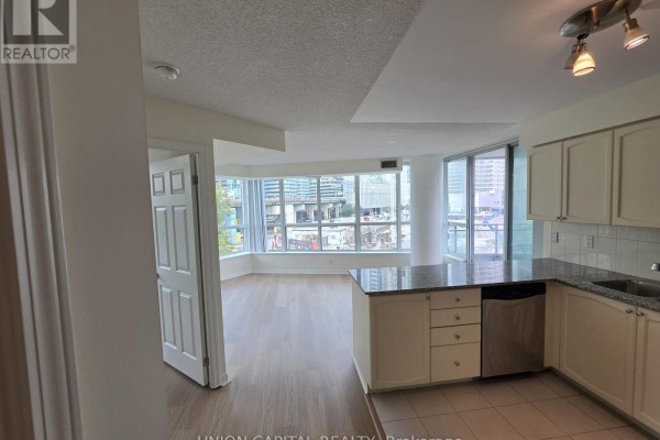 Kitchen with white cabinets and granite counters opens to living area with large windows. - 302 - 228 Queens Quay W, Toronto