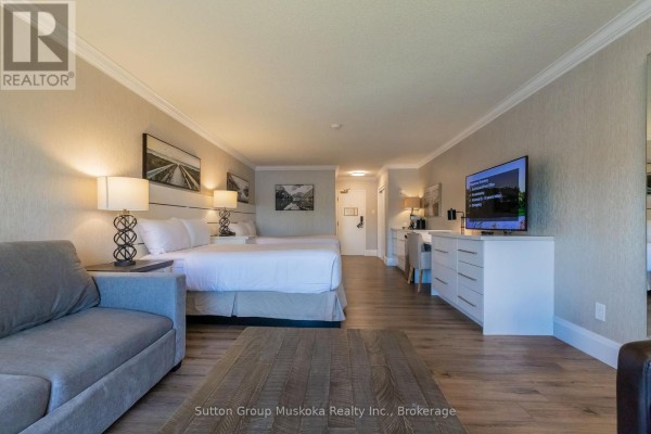 Bedroom area with two queen beds, sofa, television, desk, and wood plank flooring. - 302 - 302 Bayshore - Deerhurst Drive, Huntsville