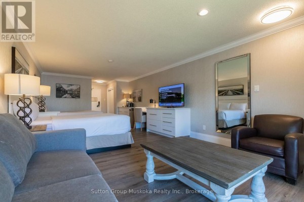 Resort room with two queen beds, sofa, television, desk, armchair, and mirror reflection. - 302 - 302 Bayshore - Deerhurst Drive, Huntsville