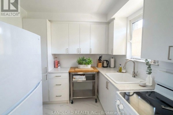 White kitchen with white cabinets, a stainless steel sink, and white countertops. - 302 - 36 Wood Glen Road, Toronto