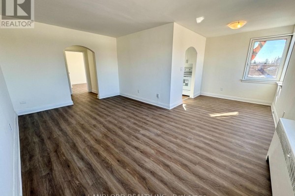 Living room with dark wood laminate flooring, white walls, and a window. - 302 - 36 Wood Glen Road, Toronto
