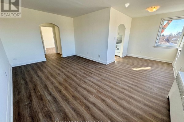 Living room with dark wood laminate flooring, white walls, an arched doorway, and a window. - 302 - 36 Wood Glen Road, Toronto