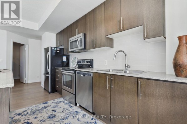 Modern kitchen with dark wood cabinets, stainless steel appliances, and a light stone countertop. - 302 - 3985 Grand Park Drive, Mississauga