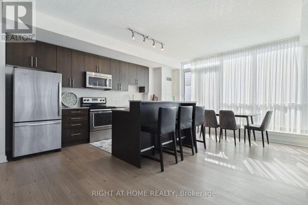 View of the kitchen island with bar stools, dining table, and open-concept living area. - 302 - 3985 Grand Park Drive, Mississauga