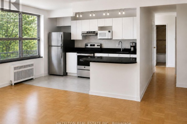 Kitchen area with white cabinets, black countertop, stainless steel appliances, and pendant lights. - 302 - 4 Sherbourne Street N, Toronto