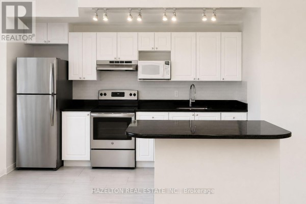 Close-up of a kitchen with white cabinets, black granite countertop, stainless steel oven, and refrigerator. - 302 - 4 Sherbourne Street N, Toronto