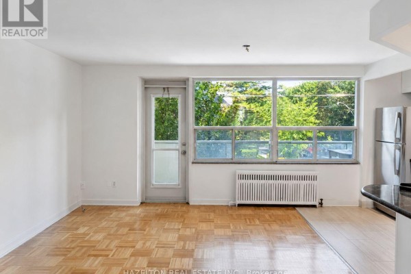 View of a living area with large windows overlooking trees, and a door to a balcony. - 302 - 4 Sherbourne Street N, Toronto