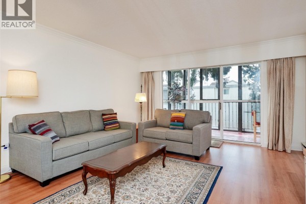 Living room area with sofas, coffee table, rug, and balcony access. - 302 1101 Hilda St, Victoria