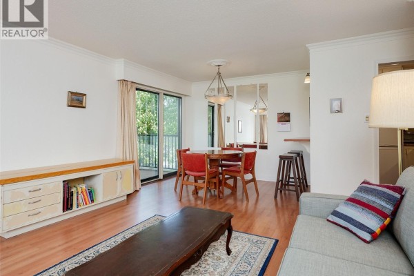 Living and dining room with built-in cabinets, dining set, and kitchen pass-through. - 302 1101 Hilda St, Victoria