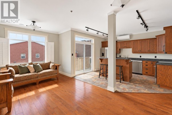 Kitchen with dark wood cabinets, stainless steel appliances, island with seating, and sliding glass doors to a balcony. - 302 111 Richmond Street, Charlottetown