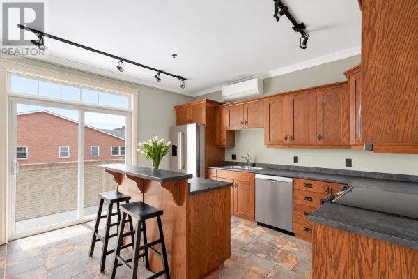 U-shaped kitchen featuring dark wood cabinets, granite countertops, stainless steel appliances, and a breakfast island. - 302 111 Richmond Street, Charlottetown