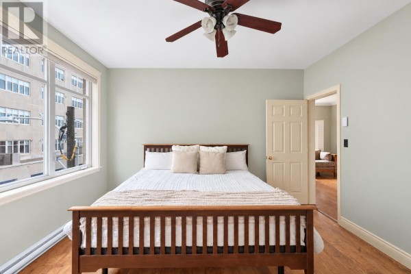 Living room and kitchen area with hardwood floors, a patterned sofa, large window, and balcony access. - 302 111 Richmond Street, Charlottetown