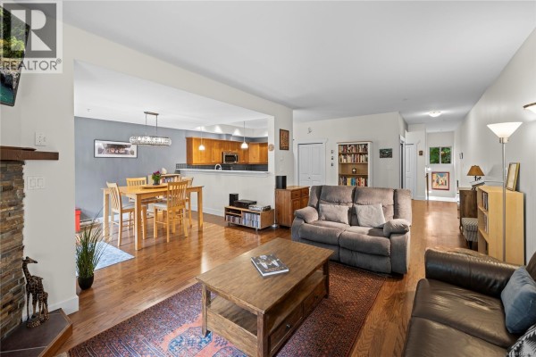 Living room with a fireplace, wood floors, sofa, and open access to a dining area and kitchen. - 302 1244 4th Ave, Ladysmith