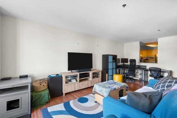 Living room with a blue sofa, entertainment center, computer desk, and a partial view of the kitchen. - 302 19721 64 Avenue, Langley
