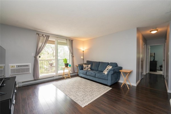 Living room with a blue sofa, television on a black stand, and dark wood flooring. - 302 470 Kenaston Boulevard, Winnipeg