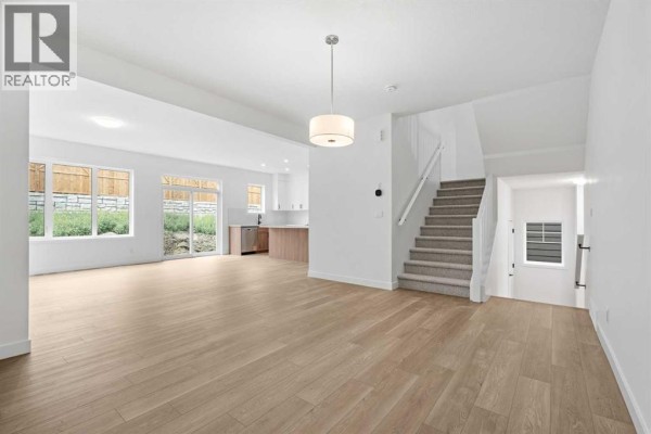 Open concept living and dining area with light wood floors, white walls, and stairs. - 302 Baneberry Way Sw, Airdrie