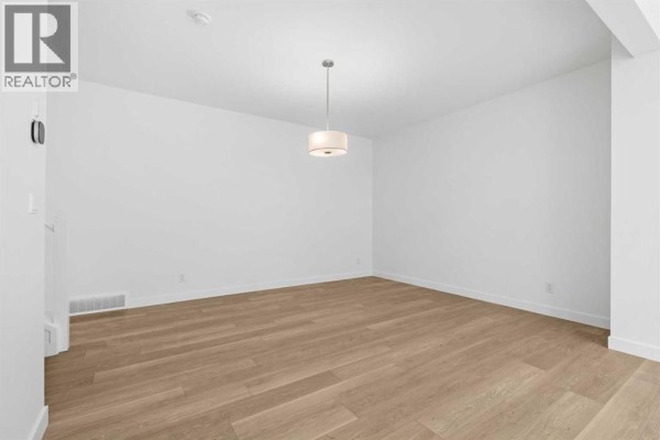 Empty dining room with white walls, a pendant light, and light wood-look flooring. - 302 Baneberry Way Sw, Airdrie