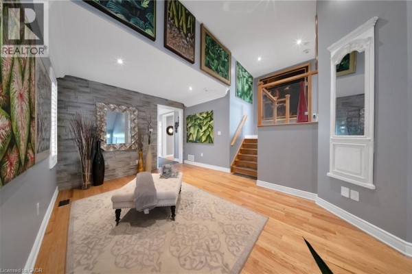 Living area with a stone accent wall, large artwork, a chaise lounge, and a patterned rug. - 302 Concession 3rd Road, Niagara On The Lake