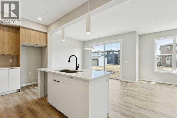 Open-concept kitchen and living area with a white island, black faucet, light wood cabinetry, and large windows. - 302 Hotchkiss Common Se, Calgary