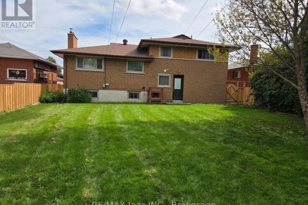 Rear exterior view of a brick house with a large green lawn and a wooden fence. - 302 Poplar Street, Oshawa